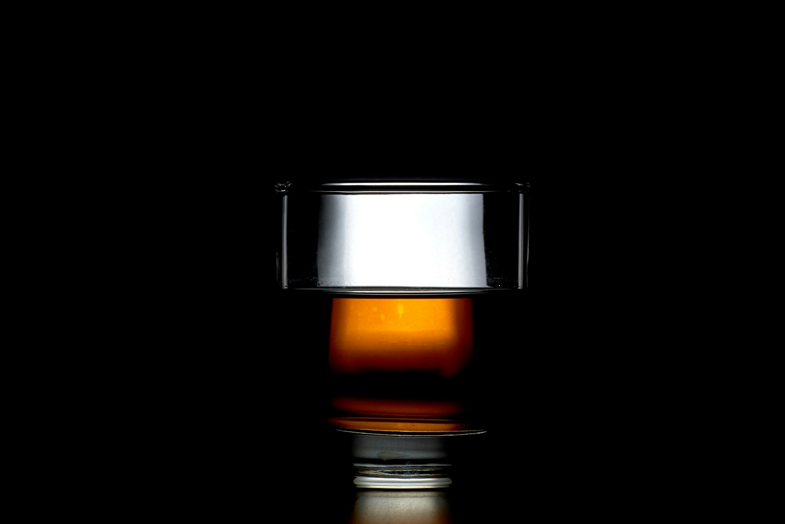 A backlit glass of whisky glowing amber against a black background.