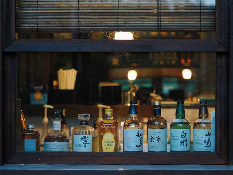 A row of Japanese whisky bottles, including Hibiki, Yamazaki, Hakushu, and Nikka Yoichi, displayed in a bar window.