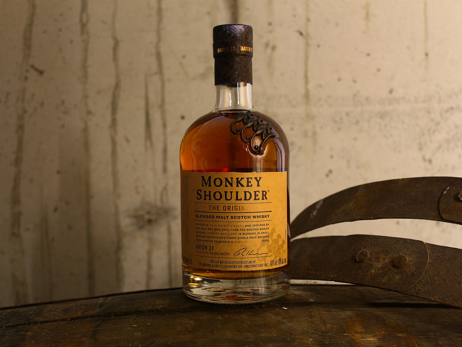 A single whisky bottle standing on top of a wooden whisky barrel.