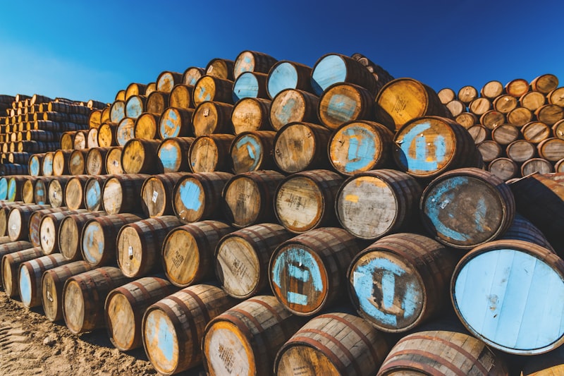 A large outdoor stack of empty wooden whisky barrels with weathered blue-painted ends, piled several rows high.
