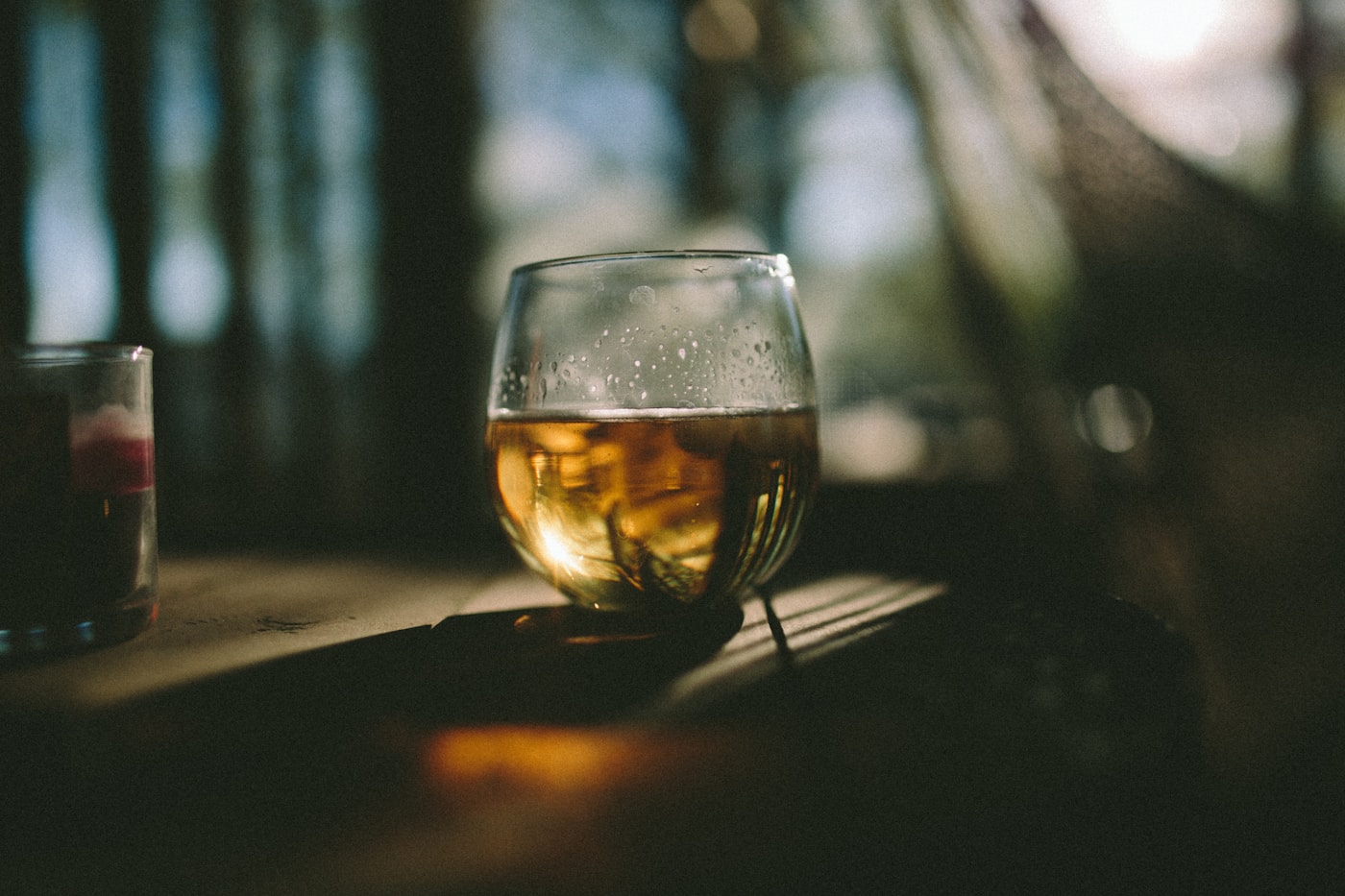 A rounded glass of amber whisky on a wooden table in warm, low light.