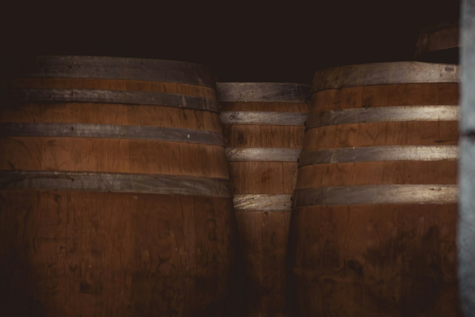 Weathered oak casks stacked in a dim maturation cellar.