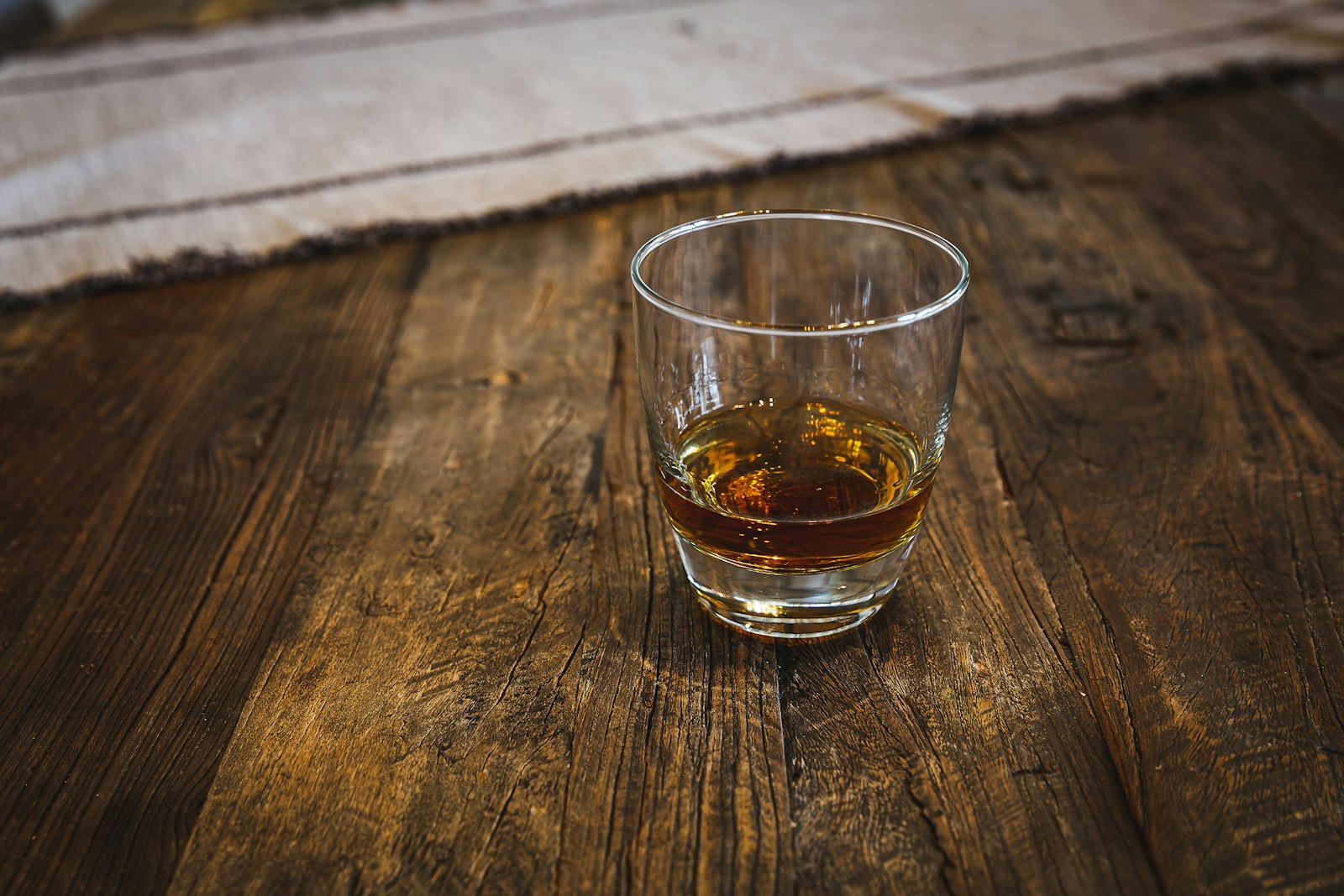 A glass of amber whisky on a rustic wooden table.