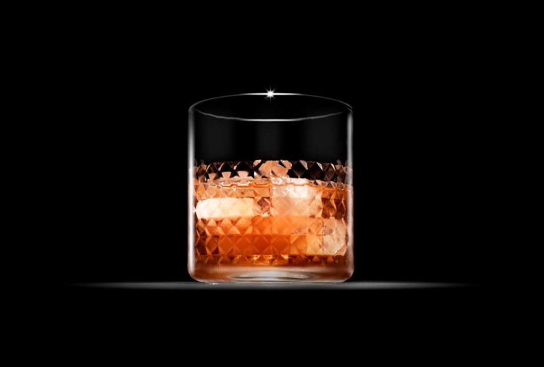 A cut-crystal glass of whisky with large ice cubes against a dark background