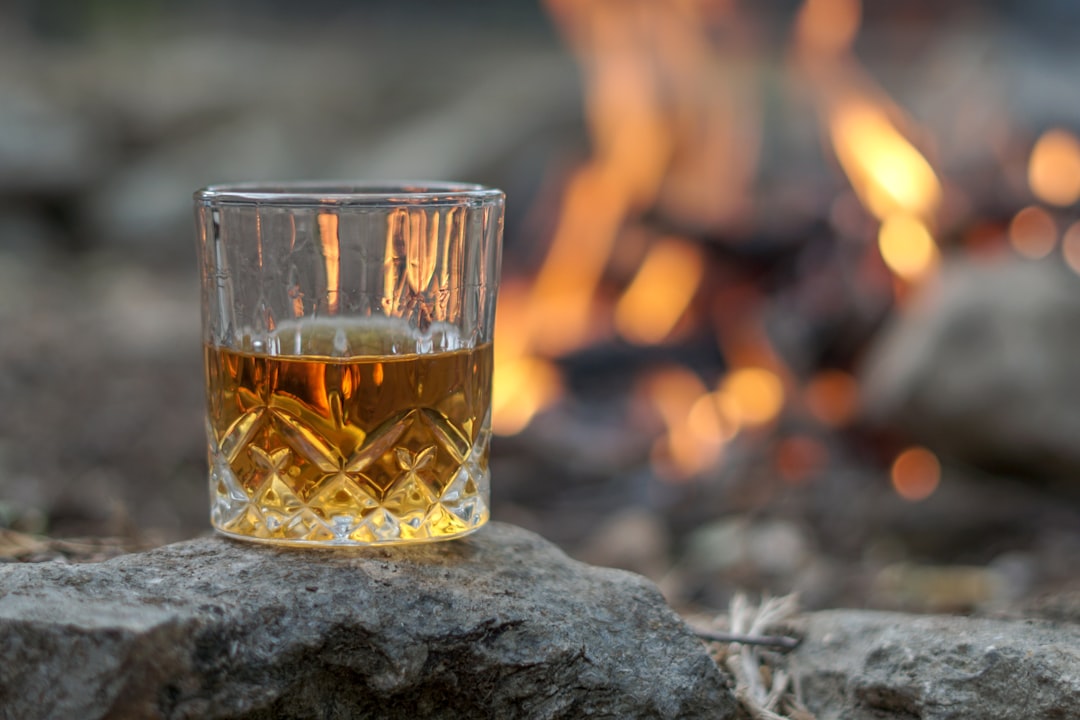 A crystal glass of amber whisky sitting on a rock beside a blurred campfire