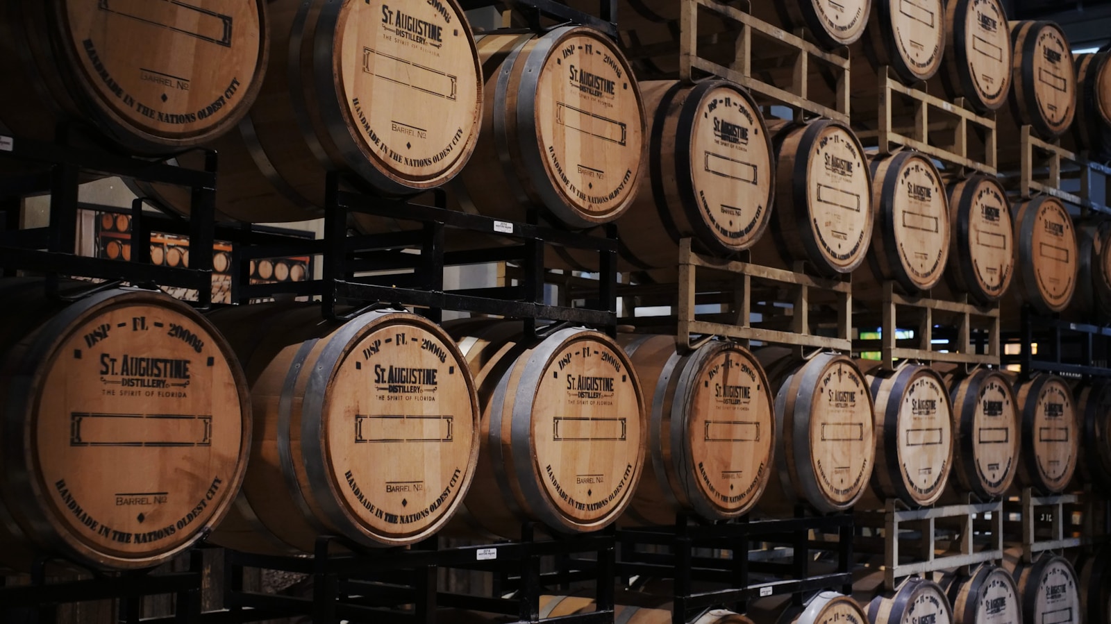 Rows of stacked oak whisky casks in a dim aging warehouse