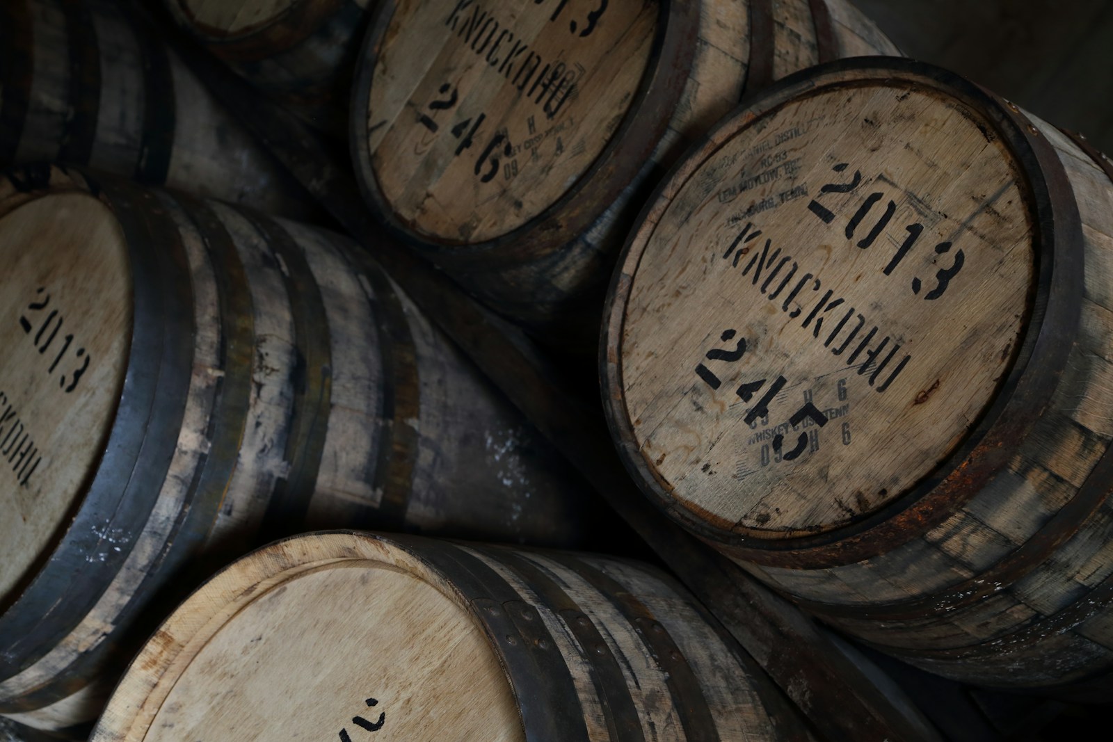 Wooden whisky barrels stacked several rows high inside a distillery warehouse