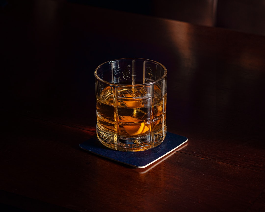 A cut-crystal glass of whisky with a large ice cube, on a dark wood table